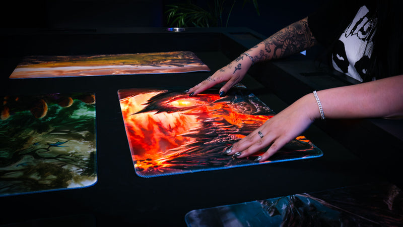 Hands gliding across the Smoldering Mountain playmat, showcasing the smooth premium surface and fiery volcanic fantasy artwork.