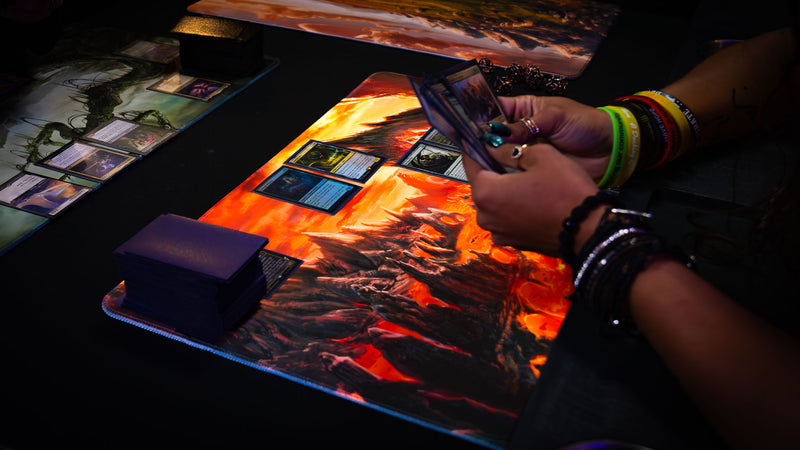 Smoldering Mountain playmat in use during a trading card game, featuring a fiery volcanic landscape with lava rivers and jagged peaks.