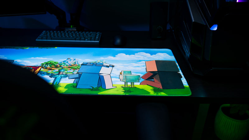 Something Like That creator deskmat featuring colorful block-style characters overlooking a floating island, displayed on a gaming desk with keyboard and PC.