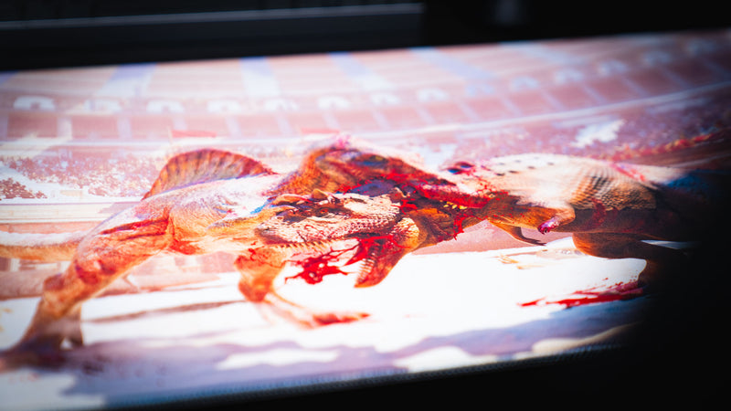 Close-up of The Spinosaurus Chompers deskmat by Keenling showcasing the detailed artwork of a Spinosaurus and Triceratops locked in a fierce battle inside a Roman gladiator arena.