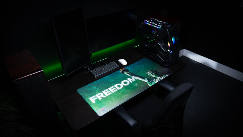 Angled view of the Statue of Liberty Freedom deskmat on a modern gaming desk, featuring bold "FREEDOM" typography, Lady Liberty raising the torch, premium HD artwork, stitched edges, and an oversized extended mouse pad.