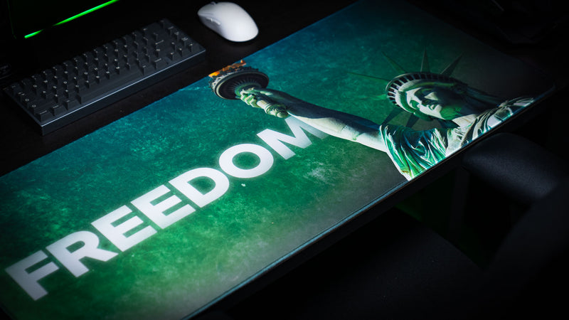 Close-up of the Statue of Liberty Freedom deskmat featuring bold "FREEDOM" typography, Lady Liberty's raised torch, vibrant HD artwork, and premium stitched-edge extended gaming mouse pad.