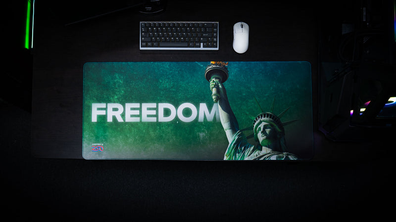 Top-down view of the Statue of Liberty Freedom deskmat featuring bold "FREEDOM" typography, Lady Liberty holding the torch, premium HD artwork, stitched edges, and an extended gaming mouse pad layout.