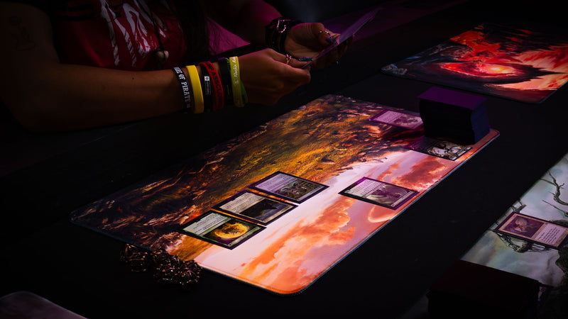Player using the Sunspire Plains fantasy playmat during a tabletop card game, showcasing golden fields, rocky terrain, and vibrant sunset skies.