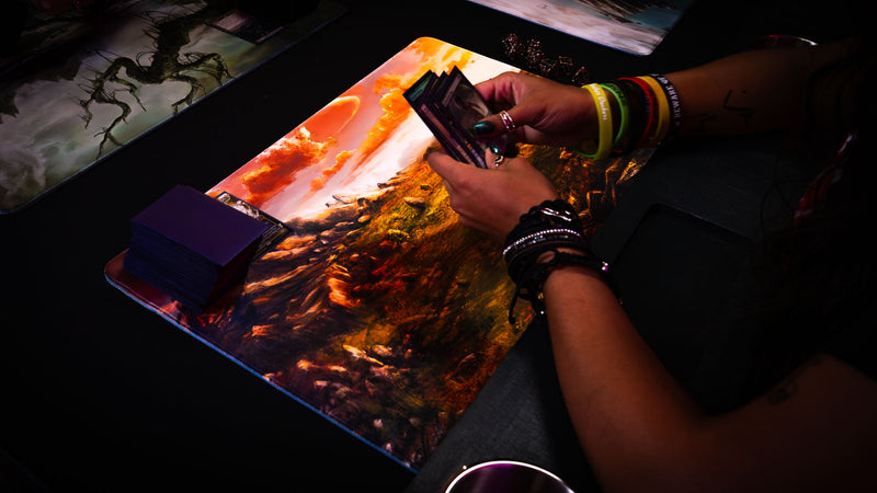 Player holding cards over the Sunspire Plains fantasy playmat during a tabletop card game, featuring golden grasslands and rocky terrain.