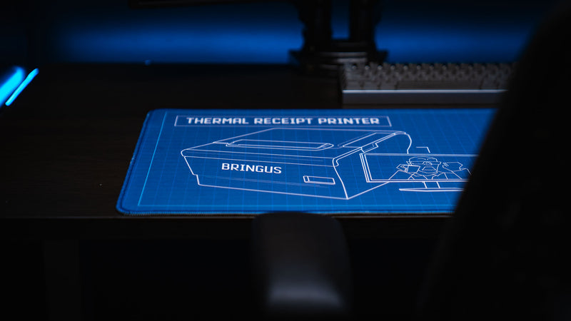 Close-up angled view of the Thermal Receipt Printer blueprint deskmat by Bringus, featuring a detailed technical line drawing on a premium extended gaming mouse pad with stitched edges.