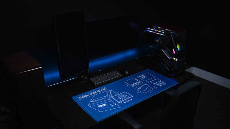 The Thermal Receipt Printer blueprint deskmat by Bringus displayed in a modern RGB gaming setup, highlighting the detailed technical blueprint artwork, extended mouse pad size, and premium stitched-edge finish.