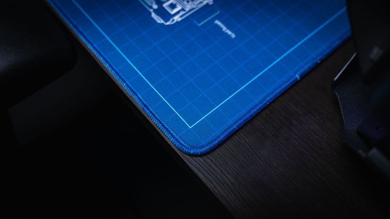 Close-up of the stitched corner and premium fabric surface of the Thermal Receipt Printer blueprint deskmat by Bringus, highlighting the durable blue stitched edges and detailed blueprint grid design.