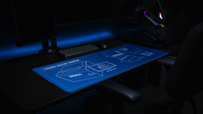Angled lifestyle photo of the Thermal Receipt Printer blueprint deskmat inspired by Rust, showcasing detailed technical schematics on a premium extended gaming mouse pad in a modern gaming setup.