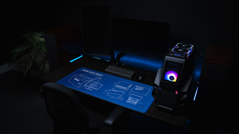 Modern gaming setup featuring the Thermal Receipt Printer blueprint deskmat inspired by Rust, showcasing a detailed technical schematic on a blue blueprint background beneath a mechanical keyboard and PC with RGB lighting.