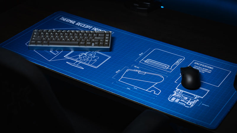 Close-up of the Thermal Receipt Printer blueprint deskmat inspired by Rust, featuring technical schematics beneath a mechanical keyboard and gaming mouse on a premium extended mouse pad with a blue blueprint design.