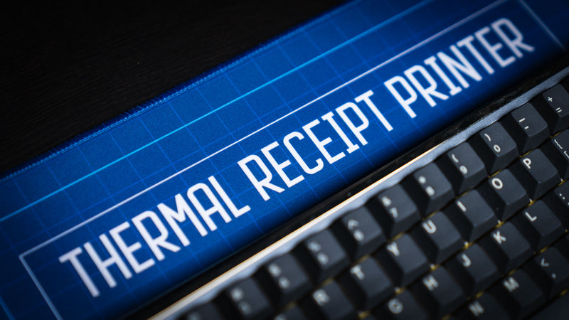 Close-up of the Thermal Receipt Printer blueprint deskmat inspired by Rust, showcasing the blueprint-style title, crisp print quality, and premium fabric surface beneath a mechanical keyboard.
