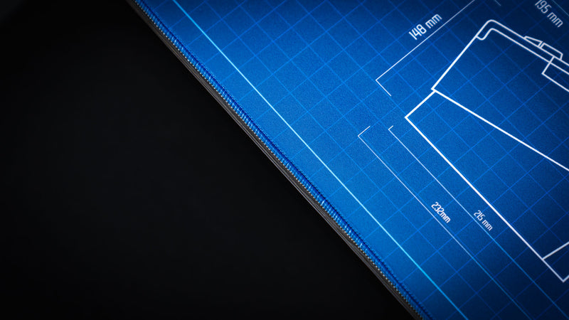 Macro close-up of the stitched edge on the Thermal Receipt Printer blueprint deskmat inspired by Rust, highlighting the premium blue fabric surface, precision stitching, and detailed technical blueprint graphics.