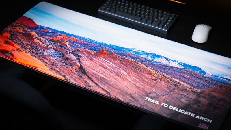 Trail to Delicate Arch deskmat featuring a panoramic view of Arches National Park with vibrant canyon landscapes, snow-capped mountains, and premium stitched edges.