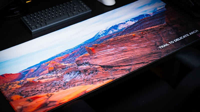 Trail to Delicate Arch panoramic deskmat showcasing sweeping sandstone formations, distant snow-capped peaks, vibrant HD photography, and premium stitched edges.