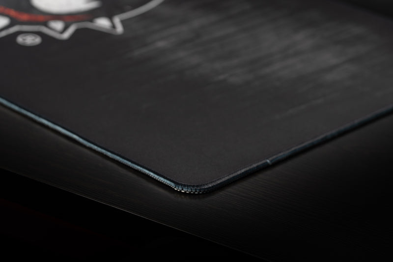 Close-up of the stitched corner and black wood-grain texture of the Georgia Mark of the Bulldog deskmat.