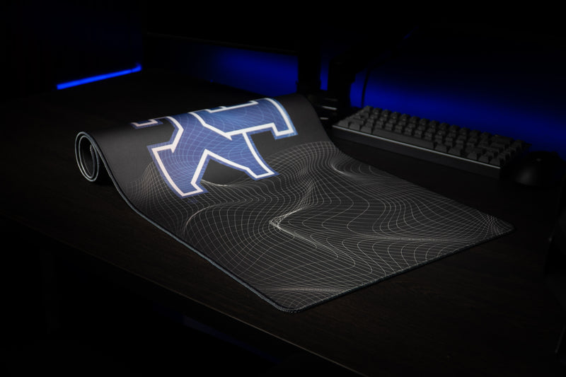 Kentucky Afterglow deskmat partially rolled beside a keyboard, showing the blue UK logo.