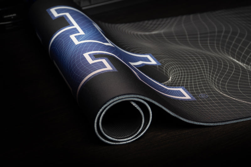 Rolled Kentucky Afterglow deskmat showing the blue UK logo and stitched edge.