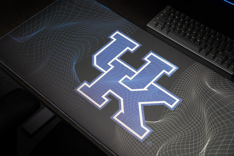 Close-up of the blue UK logo and curved wireframe pattern on the Kentucky Afterglow deskmat.