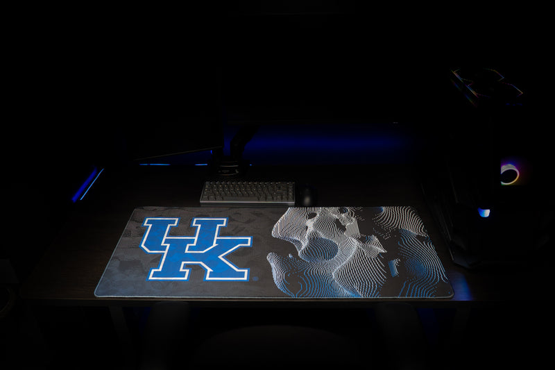 University of Kentucky Sound Wave deskmat laid flat beneath a keyboard in a dark gaming setup.