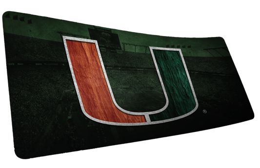 University of Miami Home Turf deskmat mockup with an orange-and-green U over a dark stadium backdrop