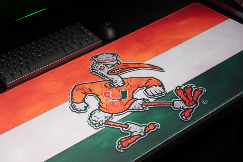 University of Miami Sebastian Pride deskmat close-up of Sebastian on the striped mat beside a keyboard