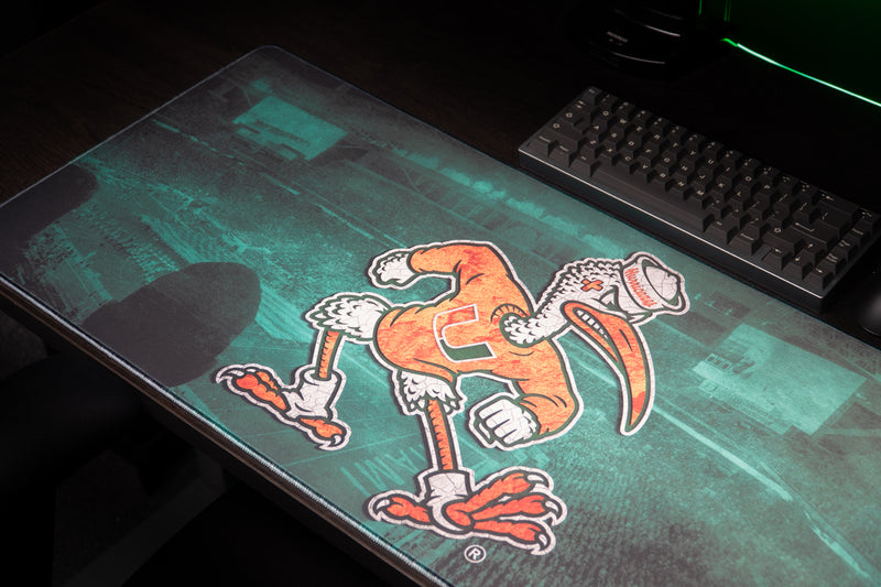 University of Miami Sebastian's Home Turf deskmat angled detail of Sebastian beside a keyboard