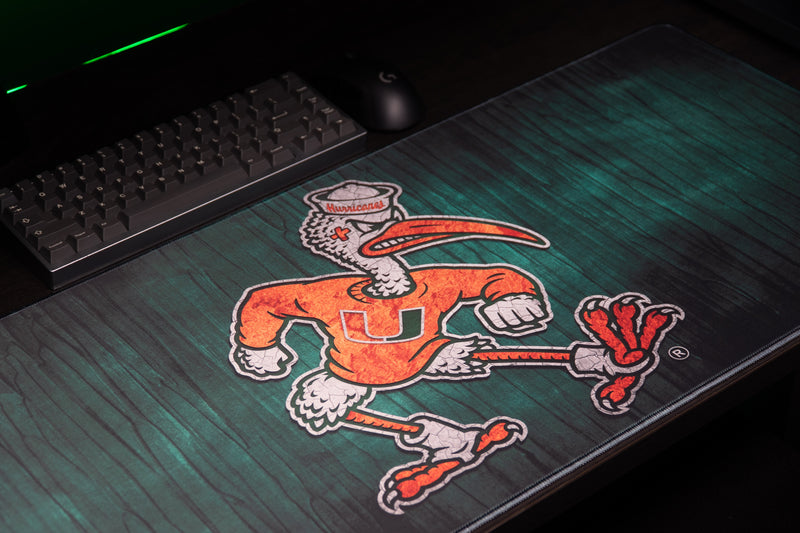 University of Miami Sebastian's Mark deskmat close angled view of Sebastian's artwork beside a keyboard