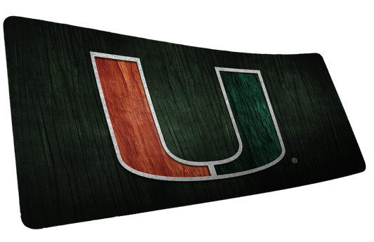 University of Miami The U deskmat mockup showing an orange-and-green U on a dark green wood-grain background