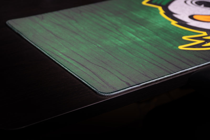Close-up of the stitched corner and green wood-grain texture on the Oregon Duck Country deskmat.