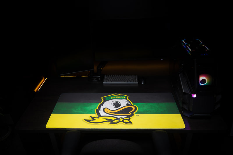 Front view of the Oregon Duck's Pride deskmat with duck mascot in a dark gaming setup.