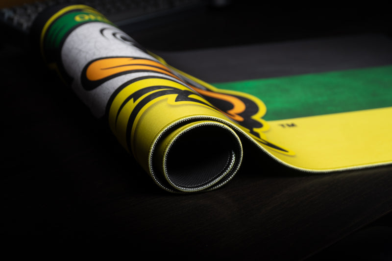 Rolled edge of the Oregon Duck's Pride deskmat showing the mascot and stitched border.