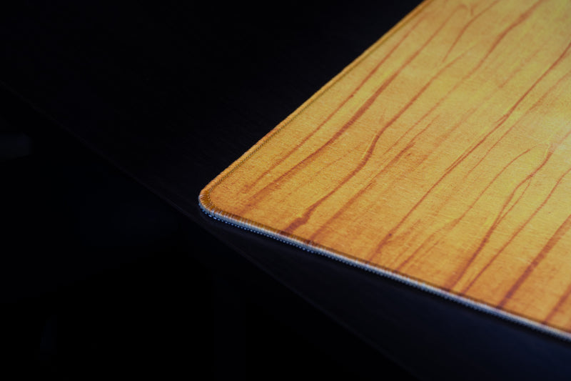 Close-up of the stitched corner and golden wood-grain texture of the Oregon Emerald Grain deskmat.
