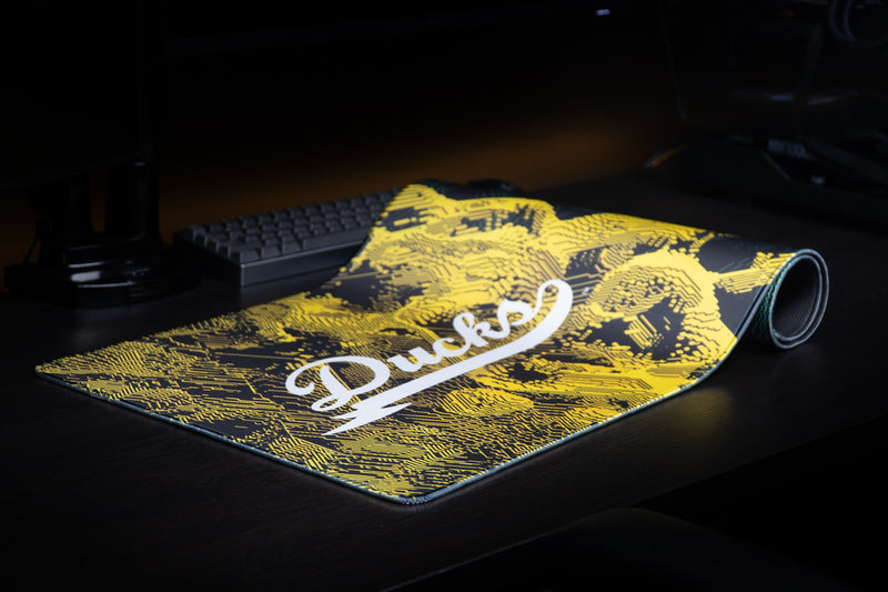 Oregon Emerald Signature deskmat partly rolled on a dark desktop, with Ducks script visible.