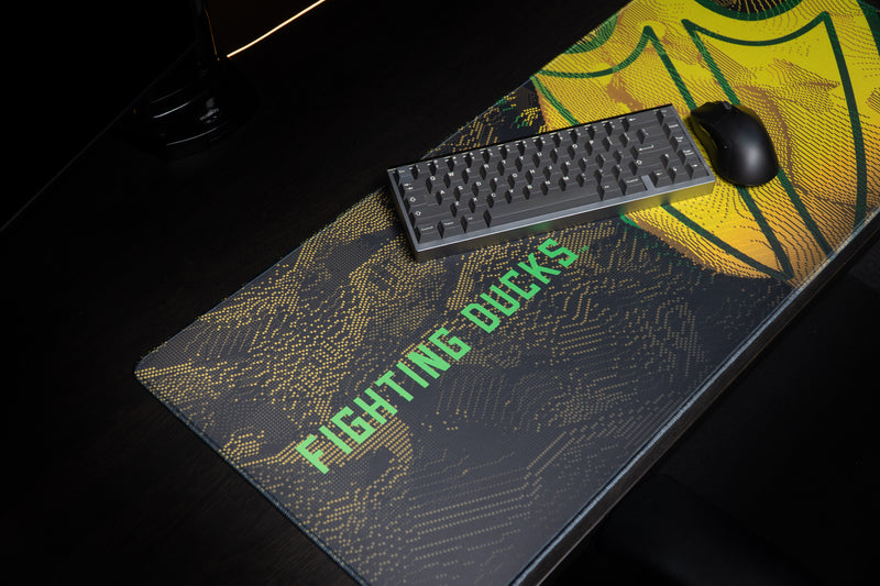 Keyboard and mouse on the Oregon Fighting Ducks deskmat beside the yellow webbed-foot design.