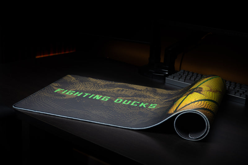 Oregon Fighting Ducks deskmat partly rolled beside a keyboard.
