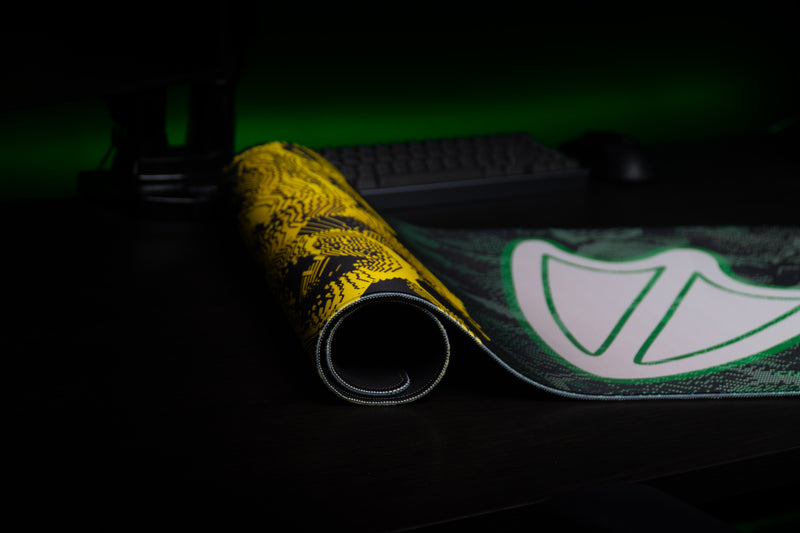 Rolled Oregon Flux deskmat showing the yellow pattern, webbed-foot emblem, and stitched edge.