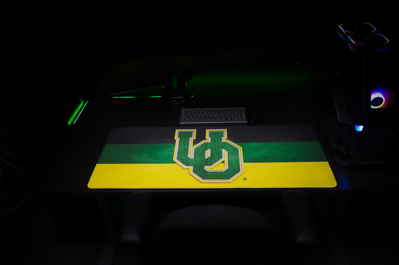 Front view of the Oregon Pride deskmat with green-and-yellow UO logo beneath a keyboard.