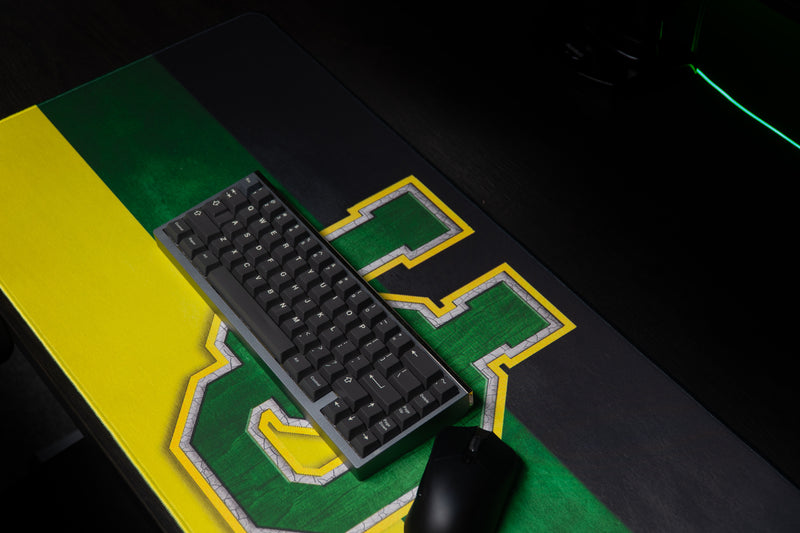 Keyboard and mouse resting on the Oregon Pride deskmat over its UO logo.