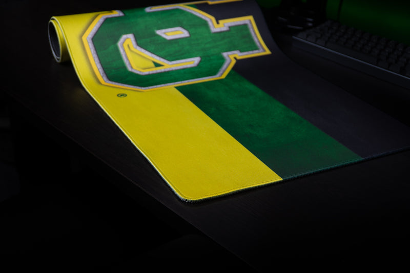 Oregon Pride deskmat partly rolled on a dark desktop, displaying its black, green, and yellow stripes.