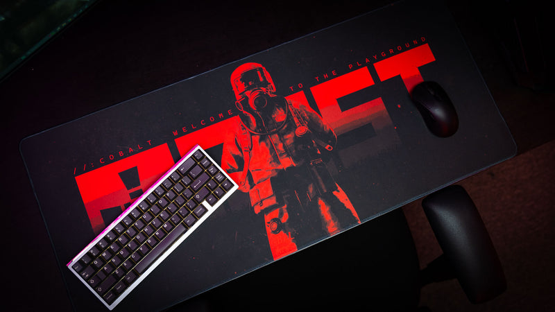 Top-down view of the Welcome to Rust full-desk mousepad featuring red hazmat artwork with keyboard and mouse in a dark gaming setup.