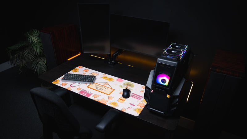Angled overhead view of the Welcome to the Leaf Pile deskmat in a cozy gaming setup with dual monitors, RGB gaming PC, mechanical keyboard, and mouse.