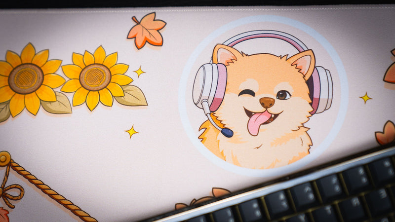 Close-up of the Welcome to the Leaf Pile deskmat featuring a cheerful dog wearing a gaming headset surrounded by sunflowers and autumn leaves.