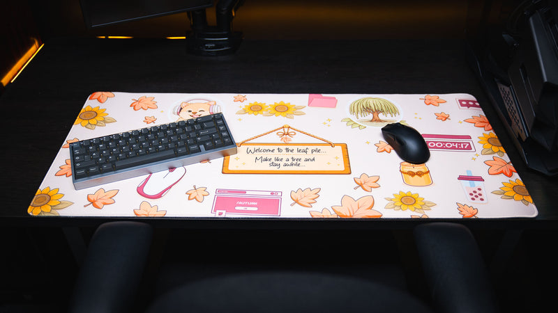Front view of the Welcome to the Leaf Pile deskmat featuring cozy autumn illustrations, decorative leaves, keyboard, mouse, and a full desktop gaming setup.
