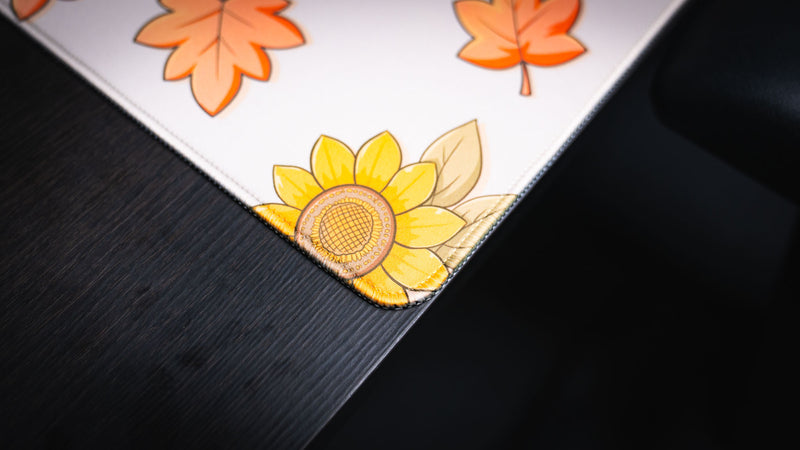 Close-up of the Welcome to the Leaf Pile deskmat featuring a sunflower illustration, stitched corner, and premium fabric edge detail.