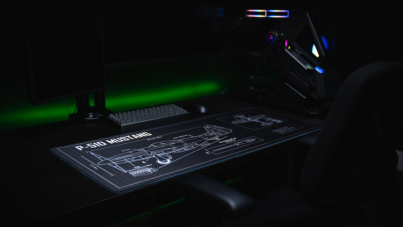 Side-angle view of the Wings of Liberty P-51D Mustang blueprint deskmat displayed on a gaming workstation, featuring detailed aircraft schematics, technical callouts, and stitched edges.