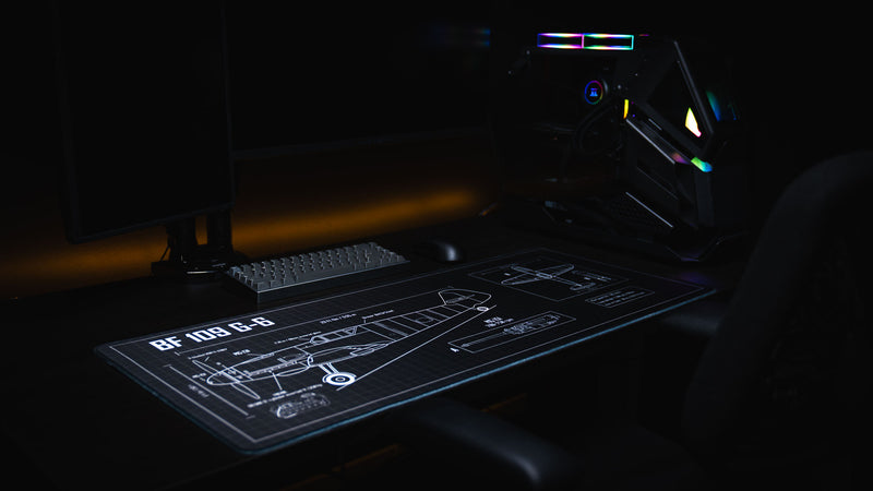 Angled gaming desk setup featuring the Wings of Steel BF 109 G-6 blueprint deskmat with a mechanical keyboard, gaming mouse, and detailed aircraft engineering schematic across the extended surface.