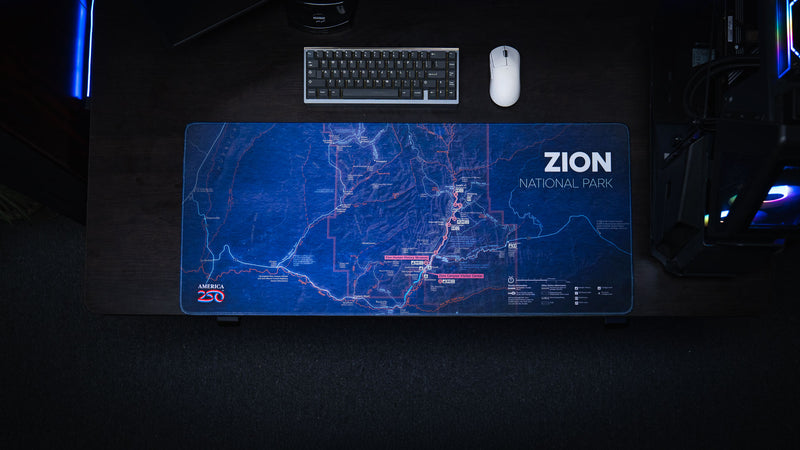 Overhead view of the Zion Map deskmat featuring a detailed blue topographic map of Zion National Park on a modern gaming desk with a mechanical keyboard and mouse.