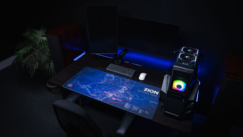 Zion Map deskmat featuring a detailed blue topographic map of Zion National Park displayed on a modern RGB gaming desk with dual monitors, mechanical keyboard, and custom PC.