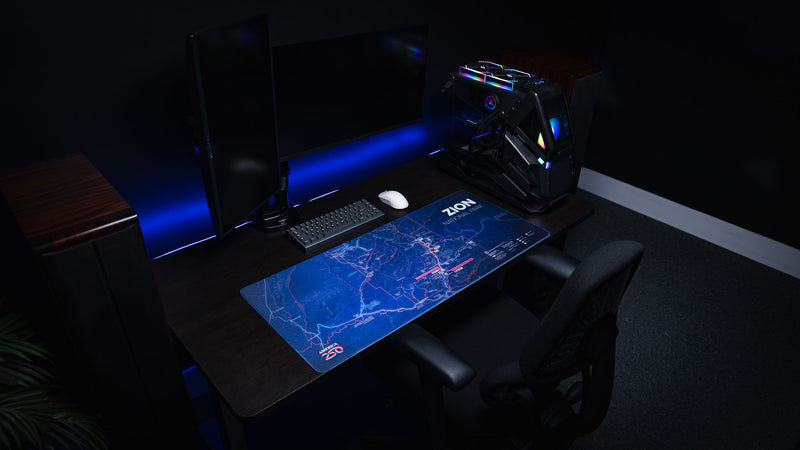 Zion Map deskmat featuring a detailed blue topographic map of Zion National Park displayed on a modern RGB gaming desk with dual monitors and a custom PC.